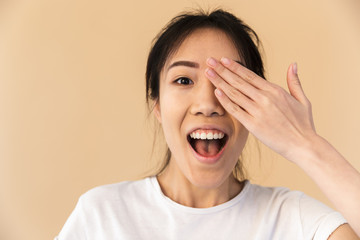 Image of happy chinese woman wearing basic t-shirt covering her eyes and peeking