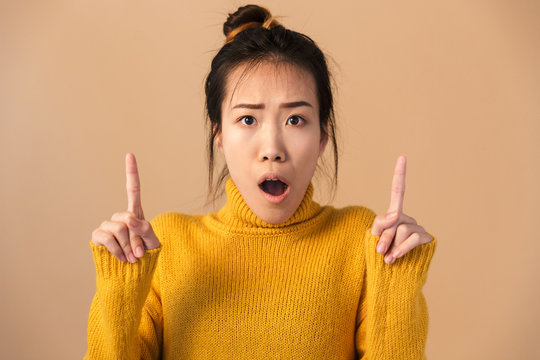 Image of surprised japanese woman wearing sweater wonder and pointing fingers upward at copyspace