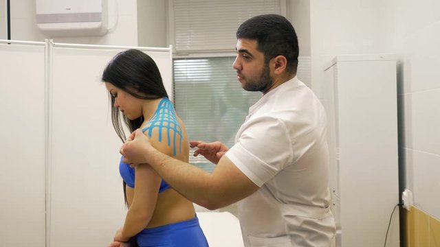 Man Applying Special Physio Tape On Woman's Back neck blue. Doctor help sport athlete recovery muscles