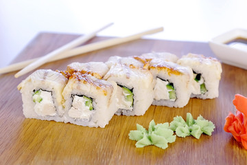 Rolls with fish and sesame seed on top served in wooden board with wasabi, ginger and soy sause