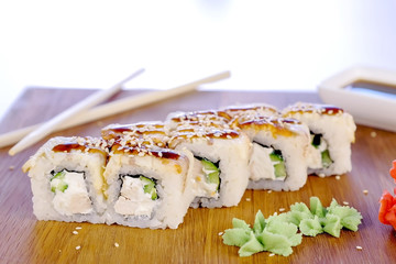 Rolls with fish and sesame seed on top served in wooden board with wasabi, ginger and soy sause