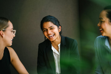 A young Asian Indian woman is having a casual business meeting with her team. They're sitting in their office while having a lively conversation.