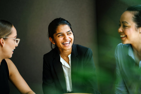 A young Indian Asian woman is having a business meeting with her team in a conference room. Her colleagues are diverse with a Caucasian brunette woman and a Chinese Asian woman