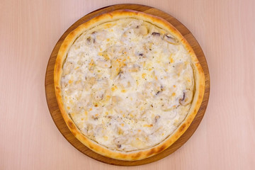 Pizza with mushrooms champignons and cheese on wooden board on the table. Close-up top view