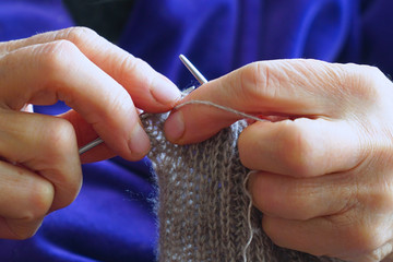 Woman knits a scarf of gray wool with knitting needles. Selective focus