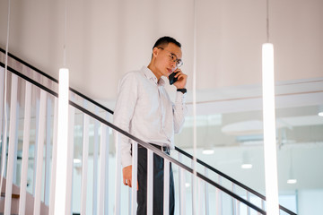 An image of a relaxed and attractive Asian Chinese man walking down the stairs during the day. He...