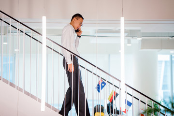 Portrait of an Asian Chinese professional walking down the steps while having a conversation on his...