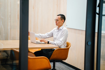 Portrait of an Asian Chinese professional man in a long sleeved shirt and pants sitting and working...