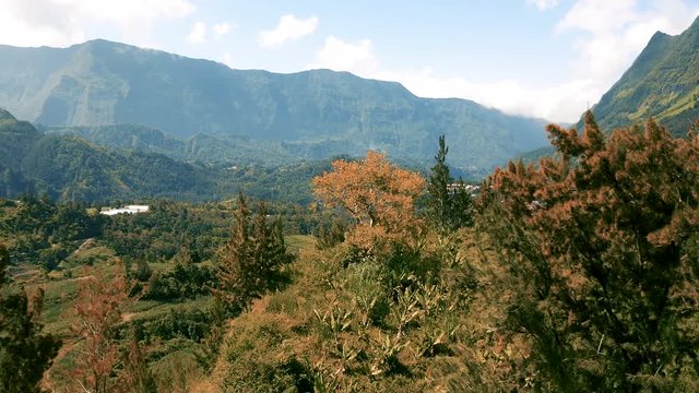 Drone flight low over trees reveals the dramatic mountain landscape surrounding the town of Hell-Bourg on Reunion Island