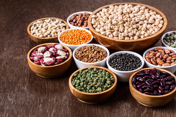 Various assortment set of indian legumes in bowls on wooden background with copyspace.