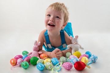 Fototapeta na wymiar Little blond kid boy coloring eggs for Easter holiday in domestic room, indoors. Child holding basket with painted eggs. Child having fun and celebrating feast with easter toy bynny