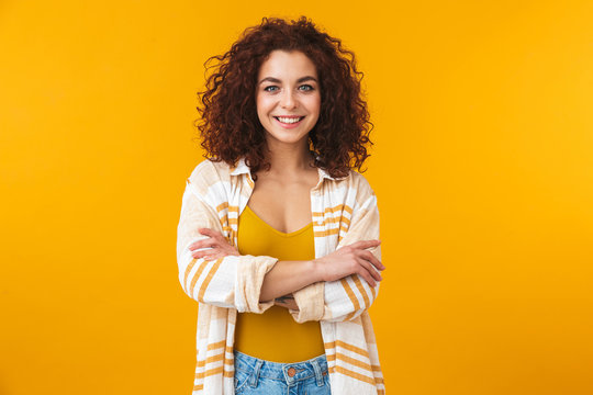 Image of young woman 20s with curly hair smiling and standing with arms crossed