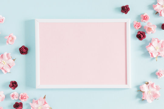 Flowers composition creative. Blank photo frame, pink flowers on pastel blue background. Flat lay, top view, copy space