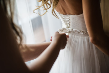 Obraz na płótnie Canvas Bridesmaid helps to wear a wedding dress