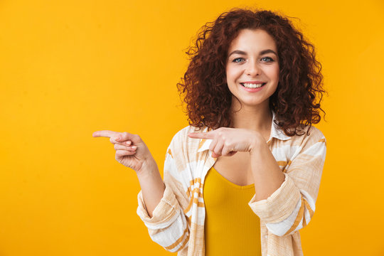 Image of bright woman 20s with curly hair smiling and pointing fingers at copyspace