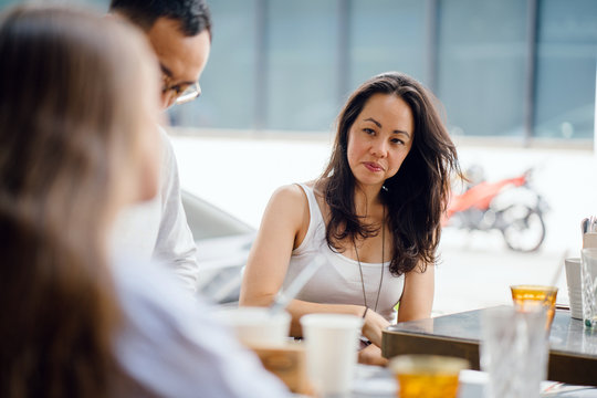 An Asian business team is consulting one another at the office during the day in an outdoor set up. All are wearing professional attire and look competent.