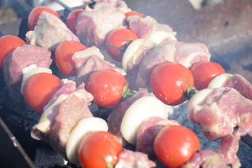 Juicy shish kebab from pork and tomatoes, fried on a fire outdoor.