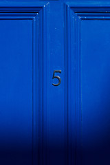 House number five in black on a bright dark blue door