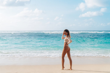 Fototapeta na wymiar Backside view of girl with sexy booty in beige colour bikini resting on deserted beach