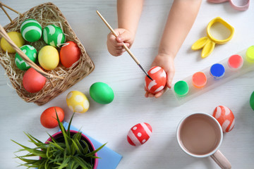 Fototapeta na wymiar Little child painting Easter eggs on wooden background, top view