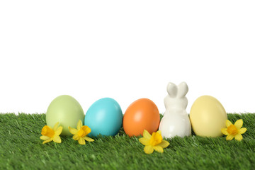 Fototapeta na wymiar Ceramic Easter bunny and dyed eggs on green grass against white background
