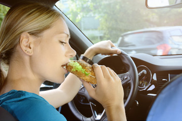 Woman as a driver eating a sandwich during a car ride and is therefore careless and distracted