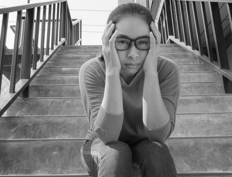 Stressed Asian woman have a headache sitting on the stairs and looking camera, woman have problem about health. Health and medical concept.  Black and white picture.