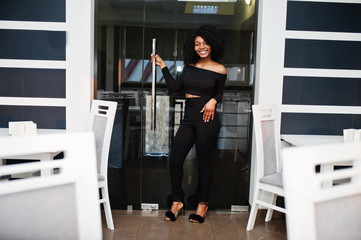 Fashionable young beautiful african american business woman with afro hairstyle wear in elegant black, stand at office near tables.