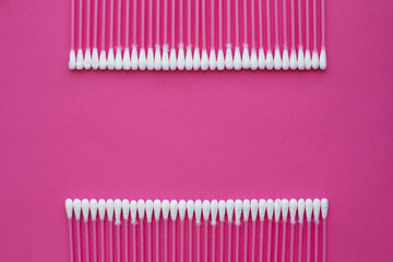 Closeup top view on cotton buds laid in a two horizontal line on pink background