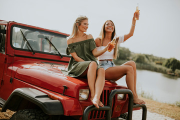 Attractive young women sitting on a convertible car by river