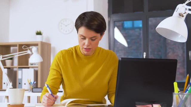 business, technology and people concept - businesswoman with laptop computer writing to notebook at office