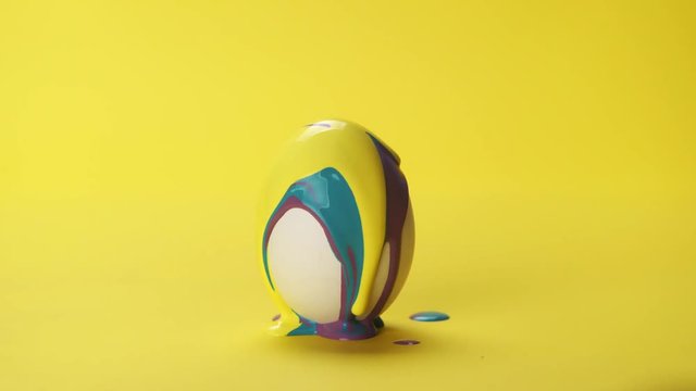 Yellow and teal color paint slow flowing on white egg on yellow background, colors mixing together. Concept Easter painted eggs, party, celebration