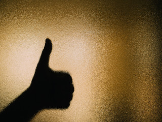 Silhouette of hand making a thumbs up on a glass.