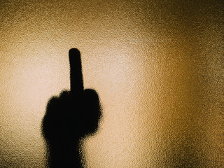 Silhouette of hand doing a fuck you on a glass.