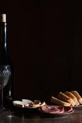 Wine bottle with wineglass and snack in black background