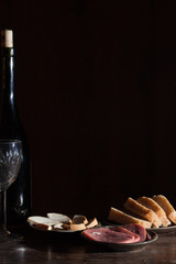 Wine bottle with wineglass and snack in black background