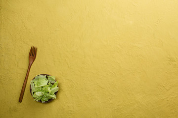 Fresh organic lettuce salad on yellow table background. Healthy food, raw and vegetarian concept with copy space.