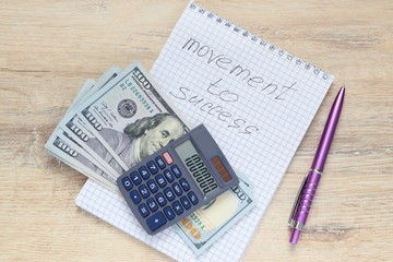 notepad with a open calculator,pen and US dollars with the inscription Movement To Success