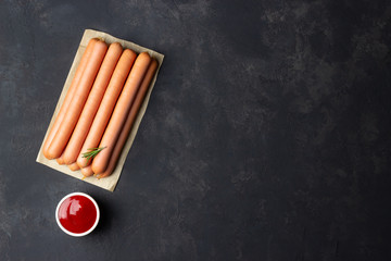 Raw sausages with ketchup on dark background. Copy space.