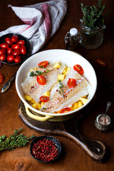 raw codfish fillet with potatoes and tomatoes in baking dish