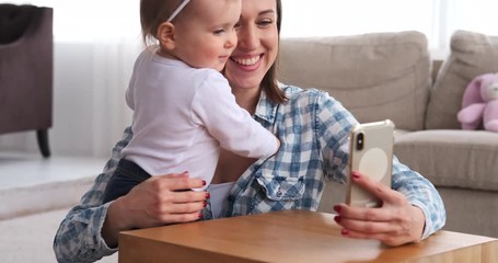 Happy mother with baby taking selfie using mobile phone camera at home