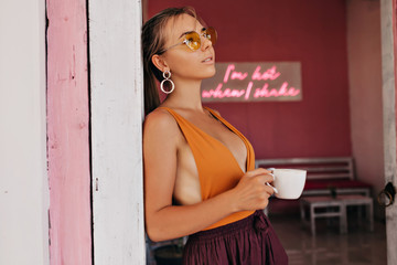 Blond woman in trendy summer outfit with a cup of coffee drinking coffee and waiting for friends 