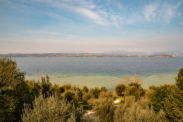 Elevated view of Lake Garda from a olive grove hill with the lake coastline on the horizon and cloudy blue sky in springtime, Sirmione, Lombardy, Italy