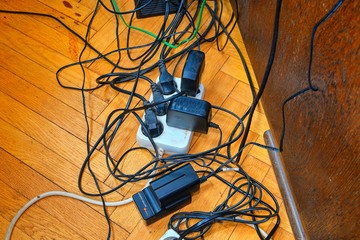 Tangled wires and battery charges on parquete floor. Domestic appliances.  Wires mess in domestic...