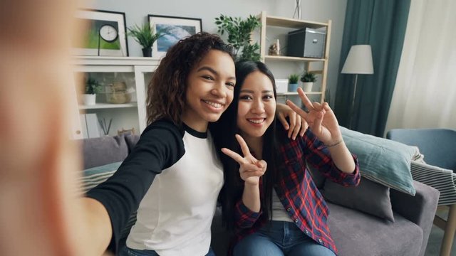 Point of view shot of attractive young ladies African American and Asian taking selfie at home posing for camera then touching screen. Photo and youth concept.