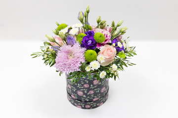 Emotional flower arrangement of various colors in a dark hat box on a light background (colors: pink, green, purple, white, lilac)
