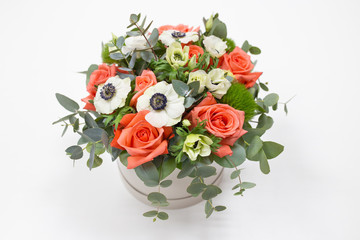 Fototapeta na wymiar Delicate floral arrangement of roses, anemones (white, pink, orange) and green eucalyptus leaves in a round white cardboard box on a bright background