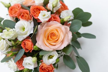 Delicate floral arrangement of roses (white, pink, orange) and green eucalyptus leaves in a round white cardboard box on a light background