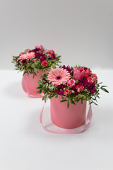 An impressive pairing composition of fresh flowers (Rose, Gerbera, Tulip) (colors: beard, pink, green, white) in a pink cardboard round hat box on a light background