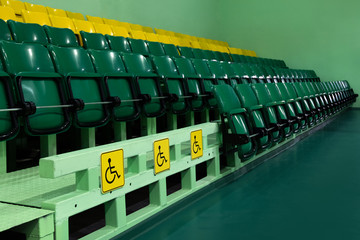 Special signs for places with disabilities. Audience for viewers. Green and yellow rows with plastic folding seats. Perspetiva. Copy space. Indoors without people.